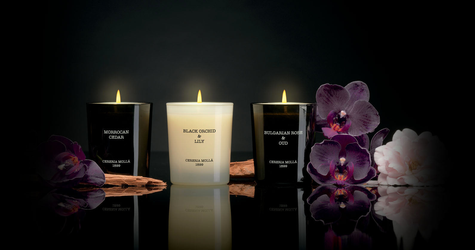 Luxury Candle Gift Set (2.4oz Bulgarian Rose-Black Orchid & Lily-Moroccan Cedar). Picture with black background surrounded by flowers.