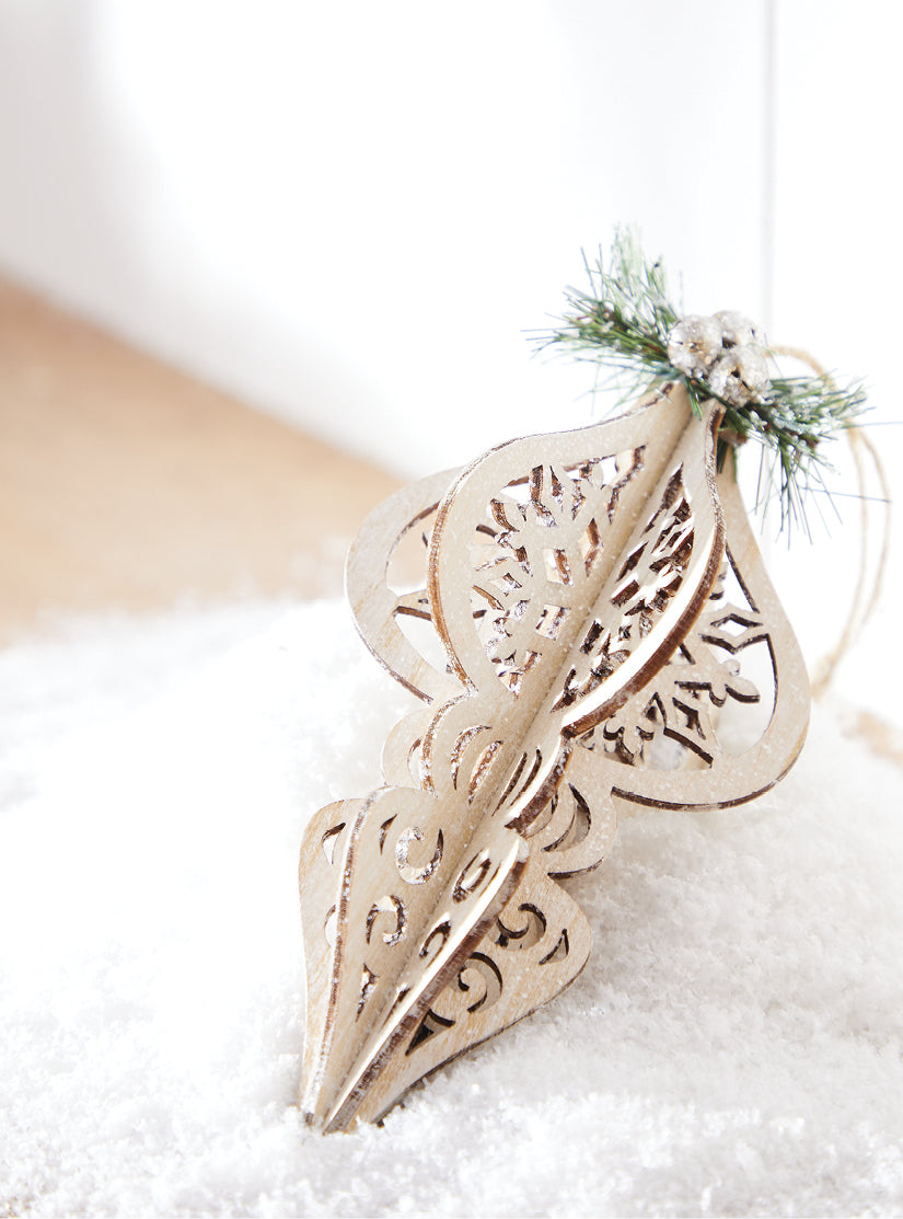 6.75" Wood Cut Finial Ornament set on a bed of faux snow. Simply lovely. Natural color. Green pine and mini silver jingle bell top detail. Jute hanging string. Made of MDF.